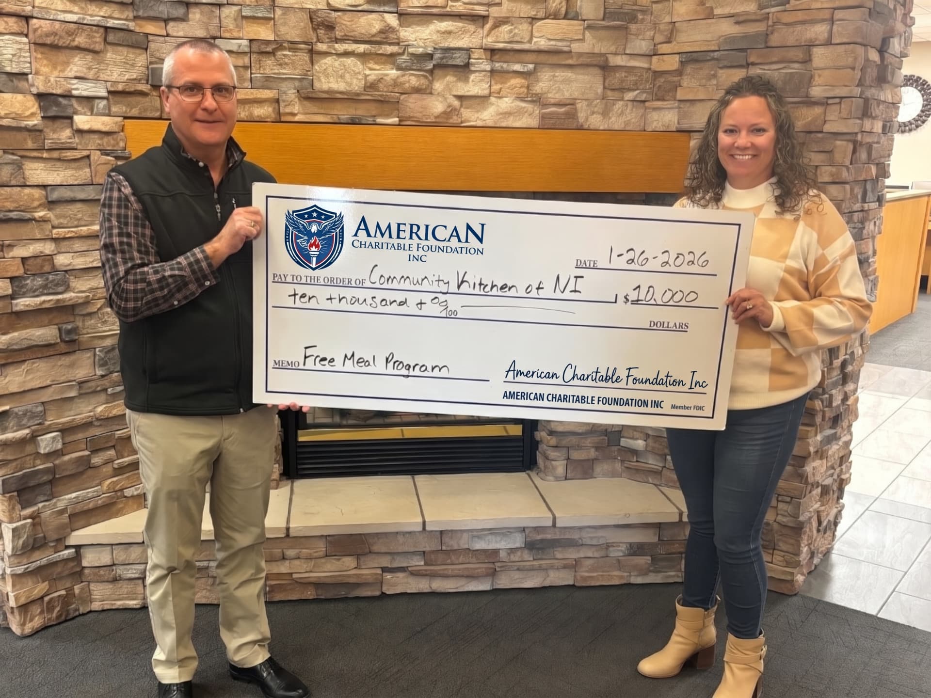 Two people presenting a large ACF grant check for the Community Kitchen of NI in front of a stone fireplace