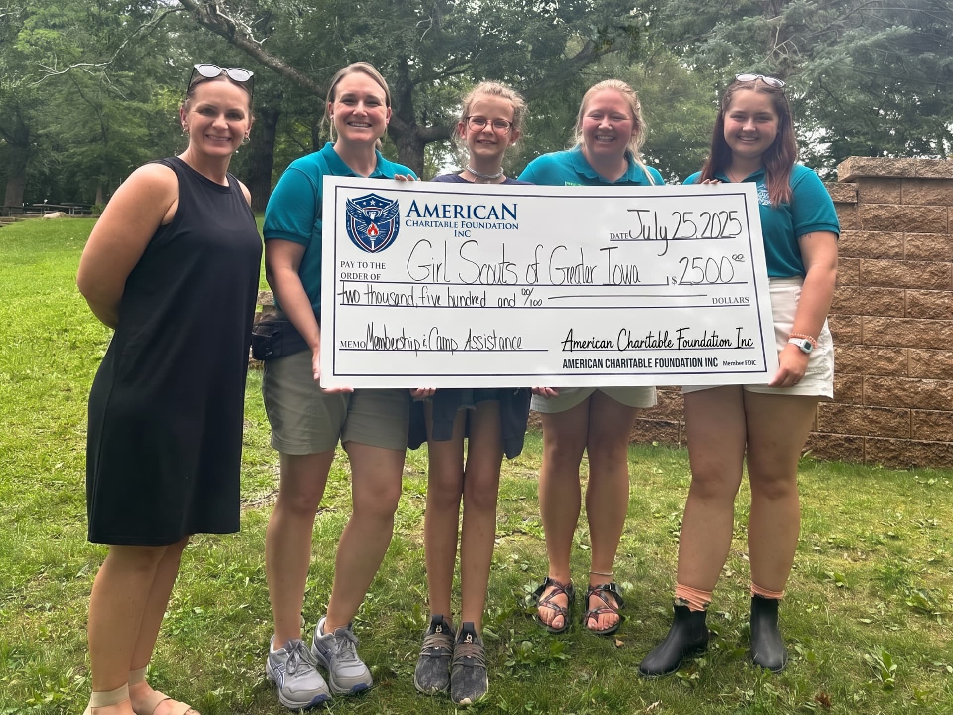 A group of five people presenting a large ACF grant check for Girl Scouts of Greater Iowa outdoors on a lawn