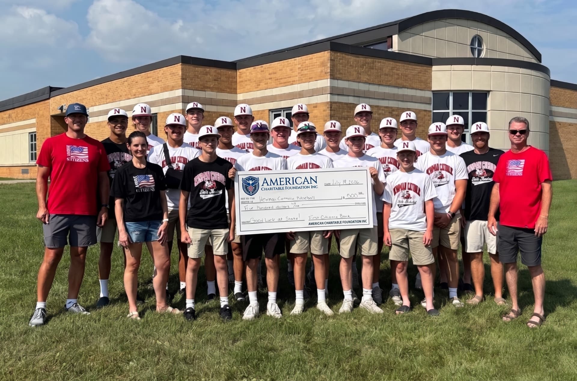 A large group of baseball players and coaches presenting an ACF grant check on the lawn of Newman Catholic