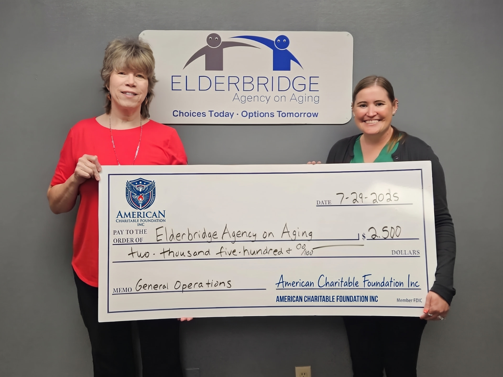 Two people presenting a large ACF grant check for the Elderbridge Agency on Aging beneath its office sign